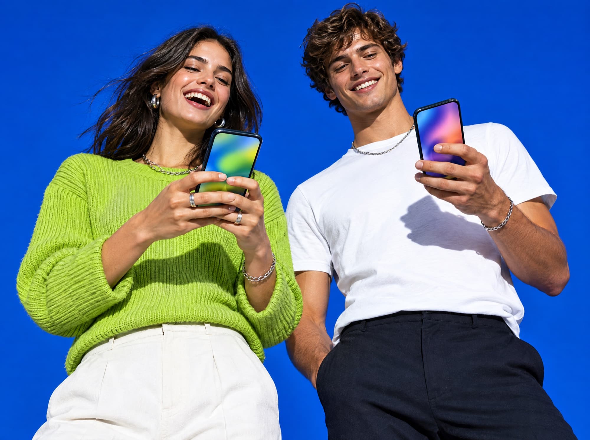 Two people laughing over their phones against an electric blue studio backdrop
